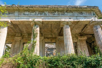 abandoned dilapidated villa in ancient Greek style: veranda colonnade with trees and bushes growing through the walls on a sunny day in early spring