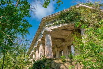 ruins of an old villa with large columns in a Greek style surrounded by bright green foliage on the trees in early spring on a sunny day in April