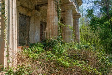 colonnade of an old abandoned dilapidated villa surrounded by the first spring bright green foliage in an abandoned park on the Black Sea coast on a sunny day in April