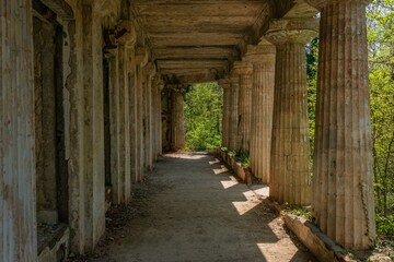 colonnade of an old villa in ancient Greek style surrounded by thickets of trees with young bright green foliage on a sunny spring day