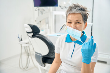 Woman dental therapist taking off protective face mask finishing work