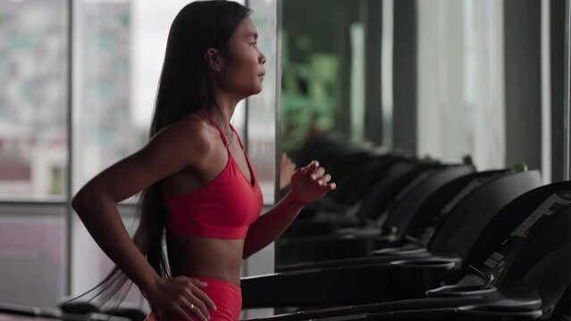 Young asian woman running on a treadmill in athletic gear in gym or fitness center