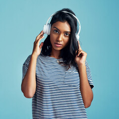 Portrait, headphones and Indian woman streaming music, audio and listening to sound on blue studio...