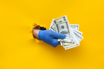 A right man's hand in a blue fabric work glove holds dollar bills (money). Torn hole in yellow paper. Concept for gastarbeiter, handyman, salary for job. Copy space.
