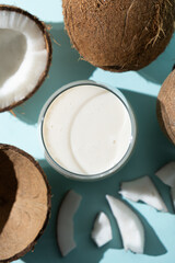 Coconut milk in a glass among coconuts on a blue background top view