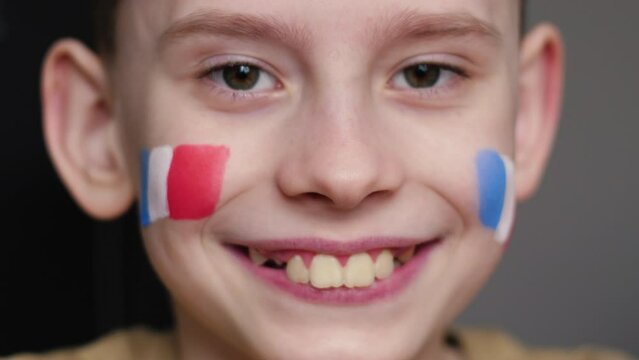 portrait of a cute smiling boy 9-10 years old with the flag of France painted on his cheek sending an air kiss while looking at the camera. young patriot, greetings from France