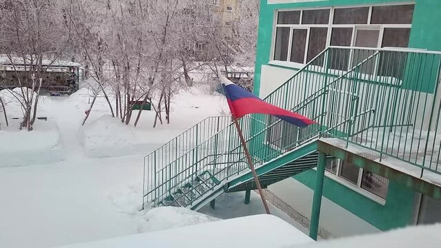 Russian flag in the snow above the entrance to the kindergarten building in winter.