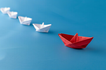 red paper boat leading other white boats on a blue background, symbolizing leader focus and strategic direction. - obrazy, fototapety, plakaty