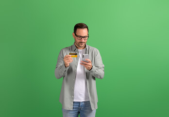 Young businessman transferring money with credit card and mobile phone on isolated green background