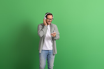 Smiling young man using mobile phone and answering calls over headphones on green background
