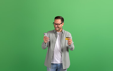 Happy young businessman using credit card to make online payment on smartphone over green background
