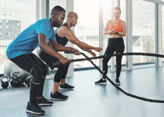 People, men and ropes for fitness in gym for workout, training and resilience for healthy lifestyle. Sports, coach and athletes exercise to target muscle, arms and shoulders with balance for strength