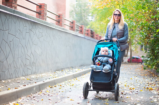 Young blond  woman with stroller going for a walk in a park