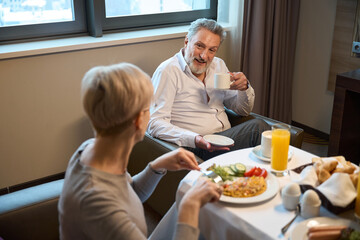 Man with cup of tea or coffee and woman having breakfast looking at each other