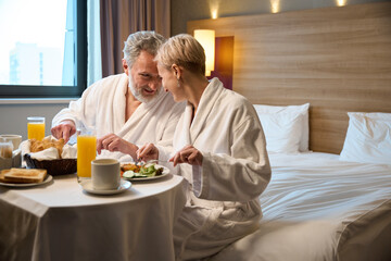 Happy mature caucasian couple having breakfast on bed at table