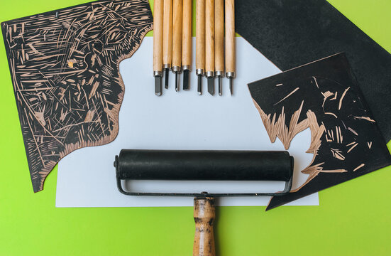 Linocut tools. Cutters, roller, black linoleum and white sheet of paper on a green background. Handicraft and design concept. Handmade creativity.