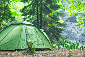 Tourist tent in forest camp. Summer camping in the mountains, spruce forest on background.