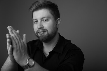 Black and white studio portrait of a caucasian male in his 20s wearing a black button up and watch. He is handsome with light hair and a beard. There is copy space. 