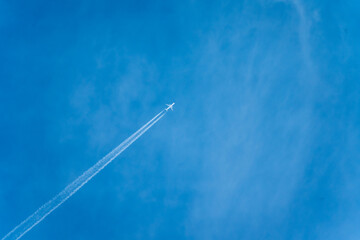 飛行機雲を引きながら青空を飛行するジェット機 - obrazy, fototapety, plakaty