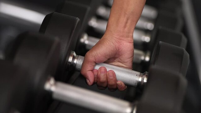 close-up hand lifting dumbbell from rack for bodybuilding and strength exercise