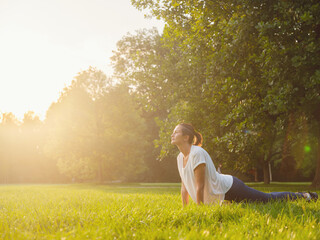 Young asian woman doing yoga in morning or evening at park, healthy woman relaxing in Upward Facing Dog Pose at city park. Mindfulness, destress, Healthy habits and balance concept