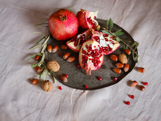 Image of Still Life with Turkish Pomegranate and olive branch on old retro plate. Dark wood background, antique copper plate. Fresh ripe whole pomegranates, opened pomegranate and seeds