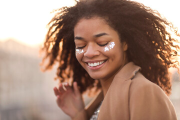 Outdoor portrait of happy joyful african american woman with shiny glitter on face and closed eyes