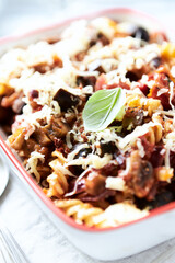 Baked pasta with cherry tomatoes, olives and mozzarella cheese. Bright wooden background. Close up.	