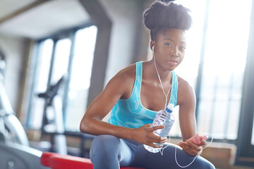 Phone, earphones and portrait of black woman in gym with water, fitness app or online subscription. Health, wellness and girl checking music playlist on smartphone with bottle, break and sports club - obrazy, fototapety, plakaty