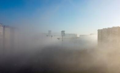 Construction cranes and a multi-storey residential building, shrouded in fog, in the early spring...
