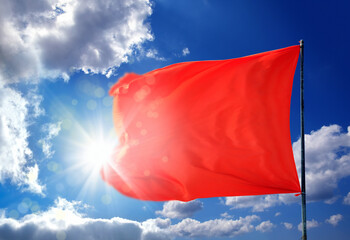 Conceptual image of waving blank red flag over sunny blue sky