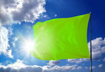 Conceptual image of waving blank green flag over sunny blue sky