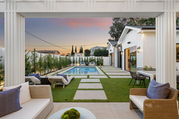 an outdoor lounge area with a pool at sunset on the left and chairs and tables