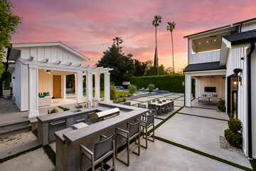 the outdoor kitchen with a fireplace, table and chairs at dusk - Powered by Adobe