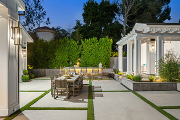 a patio with an outdoor dining table and chairs, plants and shrubs on both sides