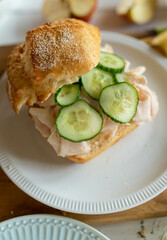 Healthy homemade breakfast sandwich bun with thin slice ham and cucumber. Served with fruits on a cutting board in the kitchen.