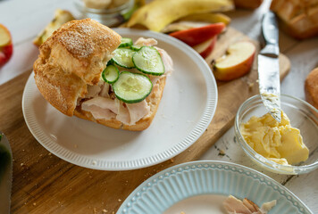 Healthy breakfast sandwich bun with thin slice ham and cucumber. Served with fruits on a cutting board