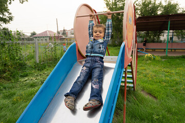 little boy rides on a slide, in kindergarten, playing on the playground, kid playing	