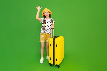 A beautiful little girl is getting ready to travel with a big yellow suitcase. A child in shorts...