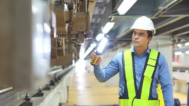 Front view professional Caucasian engineer or technician worker check and maintenance under the train with use light tube to support in train factory workplace.	