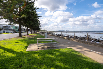 A public pedestrian walkway lined with trees, suburban houses and grass along the coast in Altona,...