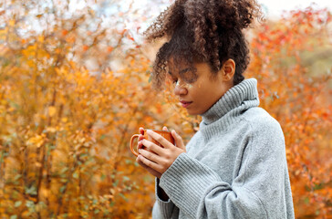 Young happy smiling mixed-race woman with coffee cup in autumn nature, pleased african american...