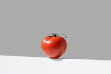 Un tomate rojo fresco sobre un soporte blanco y fondo gris