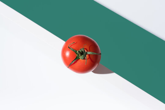 Un tomate rojo fresco sobre un soporte blanco y fondo verde. Vista superior