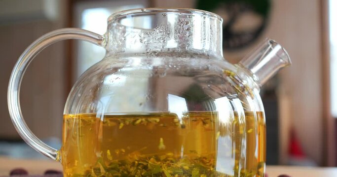 Close-up shot of teapot with natural herbal drink on table indoors. Brewing natural drink in glass teapot. Tranquility of preparing natural drink in relaxing environment. Nature concept