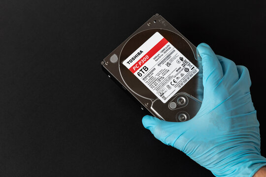 Dnipro, Ukraine - April 13, 2024: A gloved hand passes a 6 TB hard drive, a simple six terabyte 35-inch hard drive from TOSHIBA, close-up isolated on a black background.