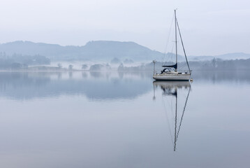 Stunning peaceful landscape image of misty Spring morning over Windermere in Lake District and distant misty peaks - 783776309