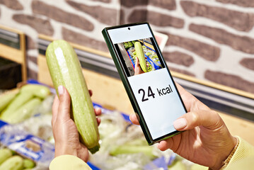 Checking calories on zucchini vegetable in store with smartphone