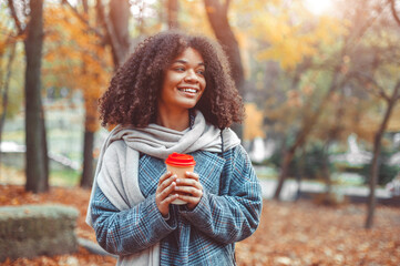 Young happy african american woman with take away coffee in beautiful autumn city park
