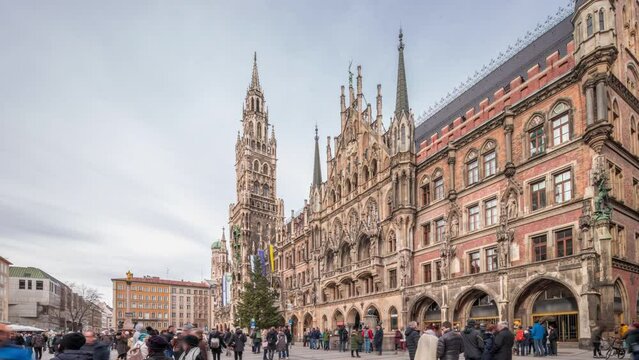 Main facade of the New Town Hall (Neues Rathaus) building at the northern part of Marienplatz timelapse hyperlapse in Munich. Fischbrunnen fountain in front. Cloudy sky. Bavaria, Germany.